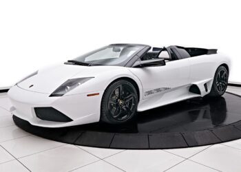 A sleek white Lamborghini Murcielago convertible with black rims is showcased elegantly on a circular platform in the showroom, exuding luxury and style.