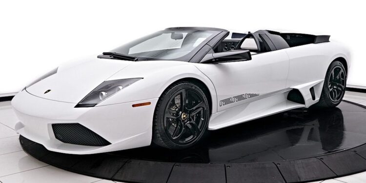 A sleek white Lamborghini Murcielago convertible with black rims is showcased elegantly on a circular platform in the showroom, exuding luxury and style.