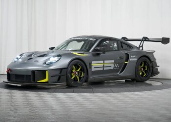 A matte gray Porsche GT2 RS Clubsport 25 race car with yellow accents, large rear wing, aerodynamic features, and the number 25 displayed on the side, is showcased in a studio setting, highlighting its race-ready design.