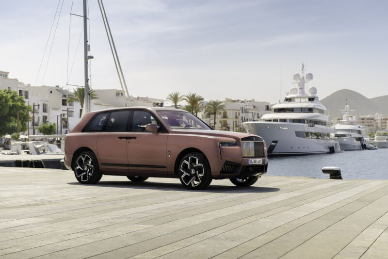 A luxury SUV, part of the impressive lineup of 2024 cars, is parked on a harbor dock with yachts and palm trees in the background under a clear sky.