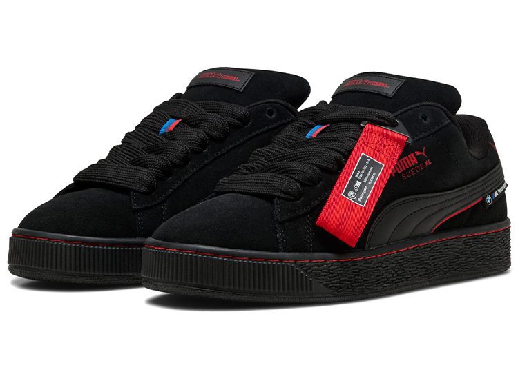 A pair of black suede Puma sneakers with red accents and a textured black sole, perfect for any 2024 fashion enthusiast. Featured in the duPont REGISTRY's Valentine's Day Gift Guide, these sneakers come with a distinctive red tag attached to one shoe, making them an ideal gift.