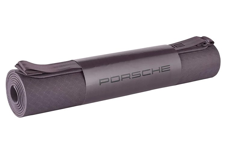 A sleek gray rolled-up yoga mat with "Porsche" elegantly printed on the center band, perfect for any duPont REGISTRY Gift Guide. Consider it an ideal choice for Valentine's Day, combining luxury and fitness in one stylish package.