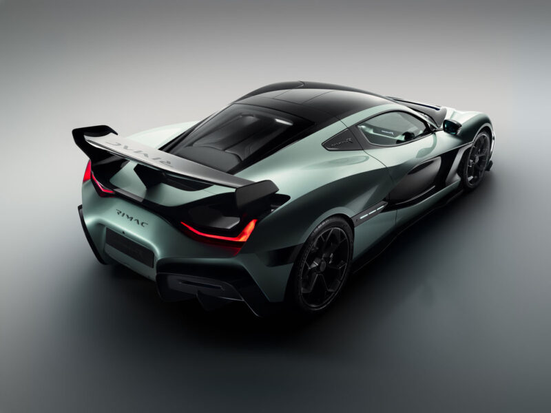 The 2024 green sports car reveals its sleek design and large rear spoiler, complemented by a stylish black roof, as seen from the rear left angle.