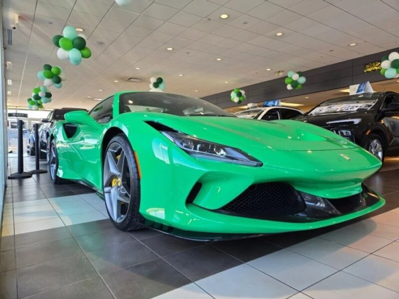 A green sports car takes center stage in a showroom decorated with green and white balloons, exuding festive St. Patrick's Day vibes as it sits among an array of other vehicles.