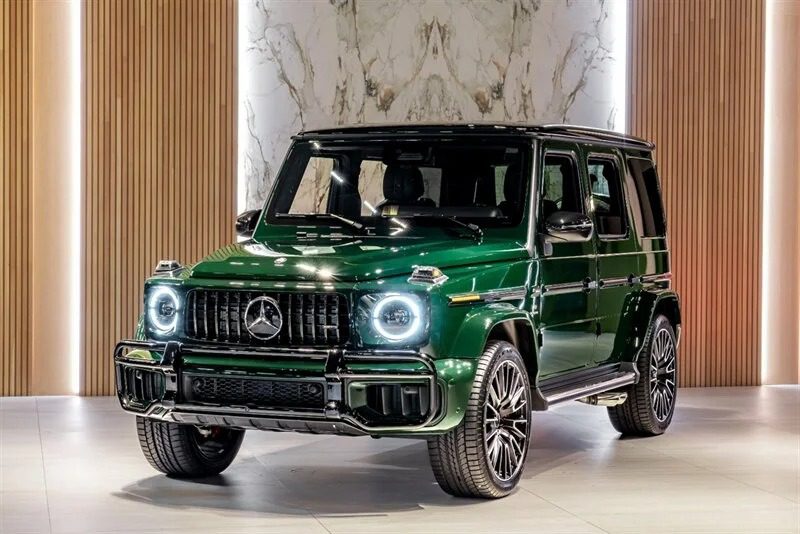 A St. Patrick's Day green Mercedes-Benz G-Class SUV is parked indoors, framed by elegant wood and marble walls. It boasts LED headlights and chrome accents, creating a harmonious blend of luxury and festive flair.