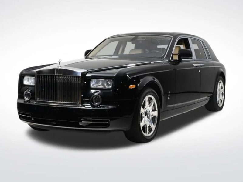 A black Rolls-Royce Phantom, the quintessential luxury sedan, boasts a distinctive front grille and emblem, set against a plain, light background.