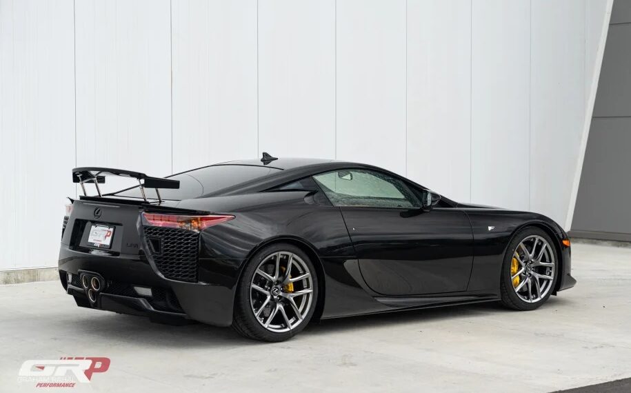 A Japanese supercar masterpiece, the black Lexus LFA boasts a sleek design, rear spoiler, and gleaming silver alloy wheels as it rests elegantly near a white wall.