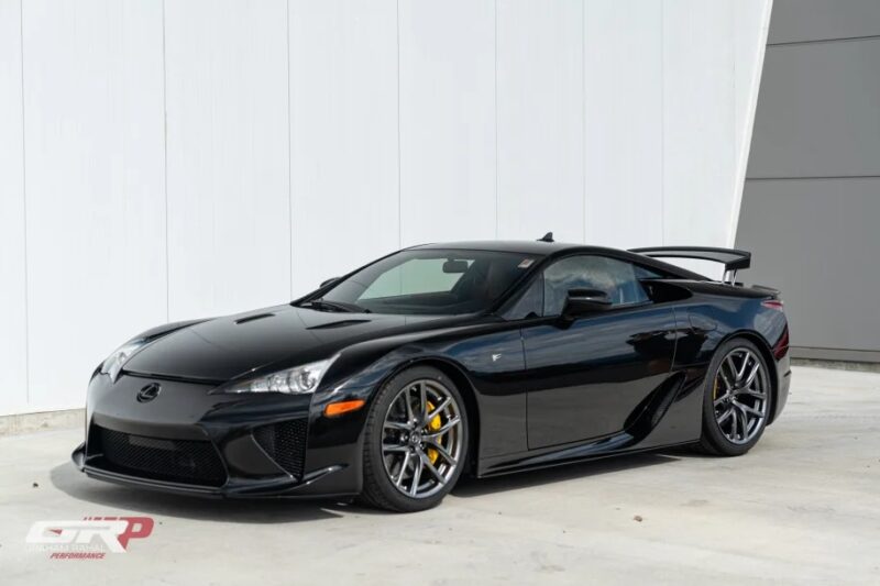 A sleek black Japanese supercar parked on a concrete surface, the Lexus LFA boasts aerodynamic curves and a rear spoiler, truly a masterpiece of design.