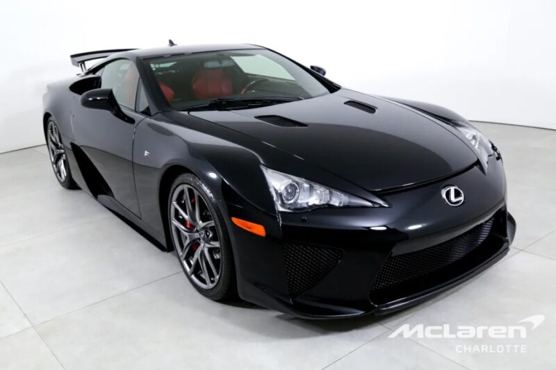 A sleek black Lexus LFA, a true Japanese supercar masterpiece, boasts a striking red interior. It's parked indoors, showcasing its distinctive headlights and rear spoiler.