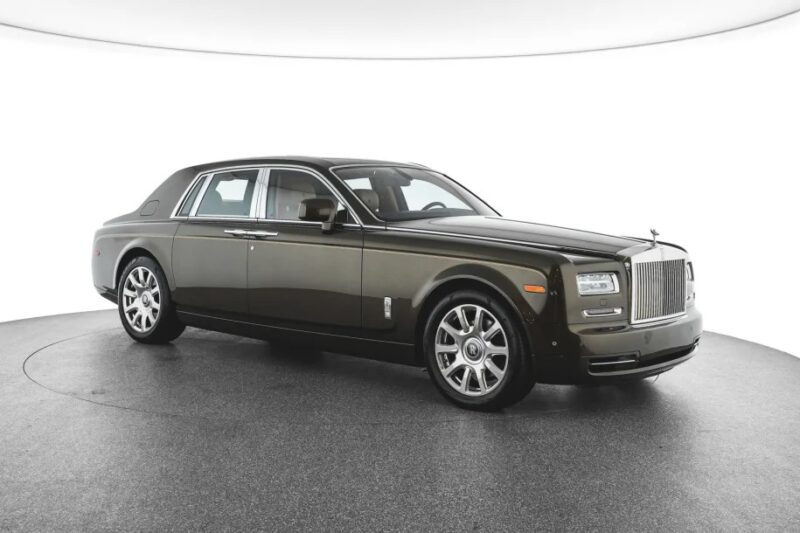 The dark-colored Rolls-Royce Phantom, a quintessential luxury sedan, elegantly sits on a rotating platform against a clean, minimalist background.