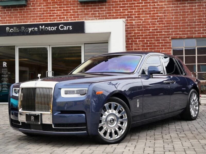 A quintessential luxury, the blue Rolls-Royce Phantom sits proudly on a brick driveway in front of the Rolls-Royce Motor Cars dealership.