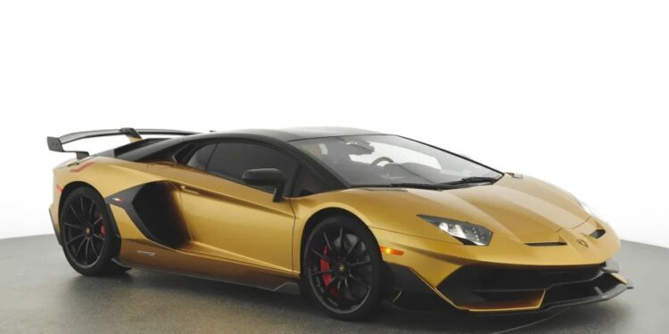 A gold Lamborghini Aventador SVJ with black accents is parked in a well-lit studio. It features a sleek design, large rear wing, and black wheels with red brake calipers. Ideal for those looking to buy the best Lamborghini.