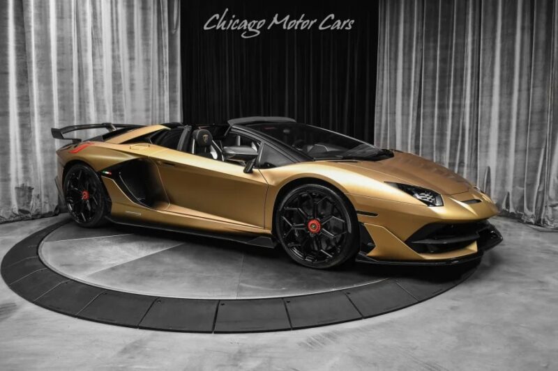 In the showroom, a gold Lamborghini Aventador SVJ with black accents and scissor doors commands attention, with "Chicago Motor Cars" in the background.