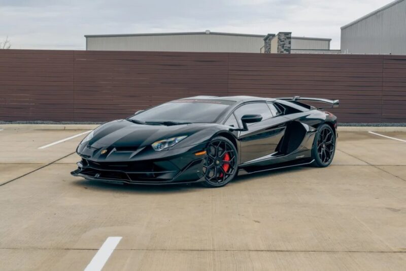 A sleek black Lamborghini Aventador SVJ with red brake calipers is parked in an empty lot, exuding irresistible allure that makes you want to buy today.