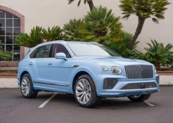 A light blue luxury SUV is parked in an outdoor area with palm trees and a white building in the background, embodying the essence of "Own The Road.