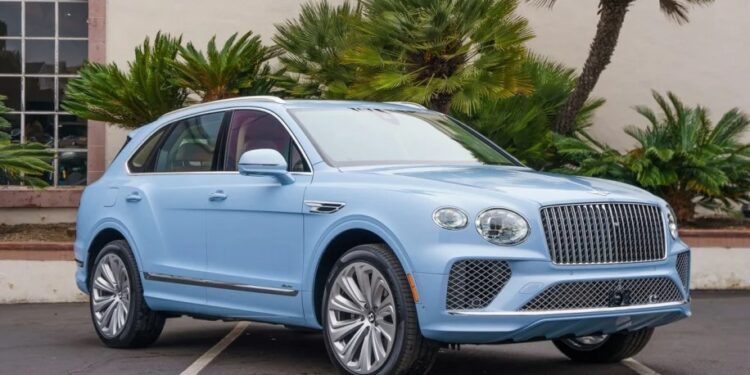 A light blue luxury SUV is parked in an outdoor area with palm trees and a white building in the background, embodying the essence of "Own The Road.