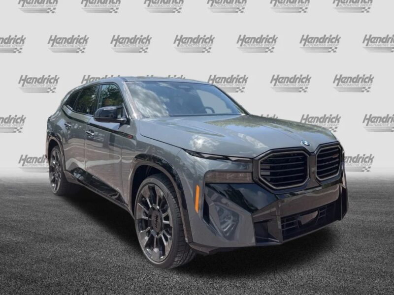 A dark gray BMW SUV, blending luxury with practicality, is parked on a lot with a Hendrick-branded backdrop.