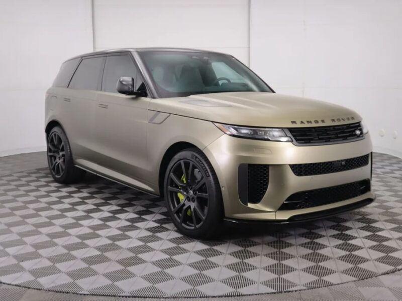 A luxury gold Range Rover SUV glistens on the checkered showroom floor, angled towards the right to showcase its performance-ready stance.