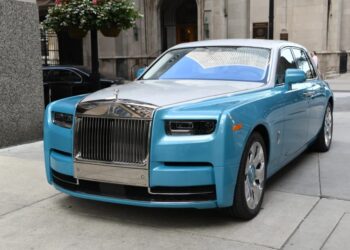 A quintessential luxury sedan, the blue Rolls-Royce Phantom is parked on a city street, showcasing its prominent chrome grille and sleek design.