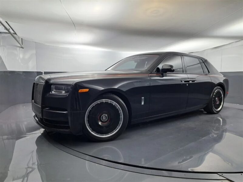 A sleek, black Rolls-Royce Phantom is parked in a brightly lit showroom, exuding quintessential luxury with its modern interior.