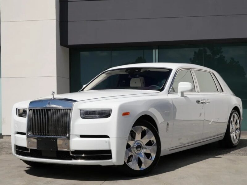 A white Rolls-Royce Phantom, the quintessential luxury sedan, is elegantly parked in front of a modern building.