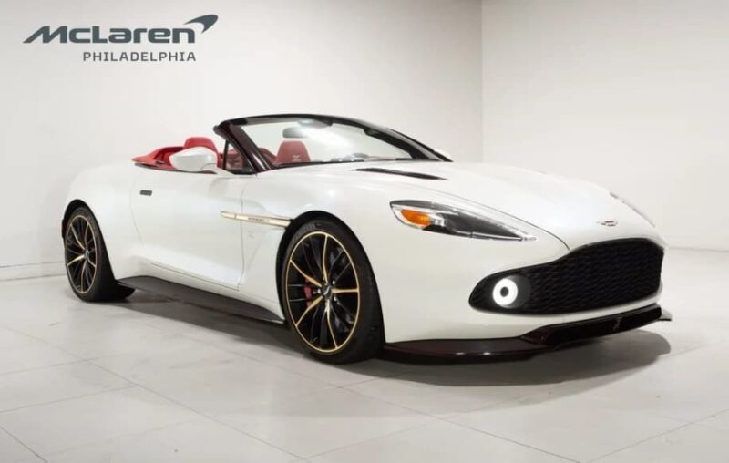 A white Aston Martin Vanquish Zagato convertible with red interior is displayed in a showroom with the "McLaren Philadelphia" logo on the wall, highlighting exclusive body styles and available now for sale.
