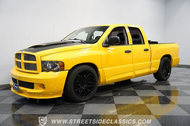 A yellow Dodge Ram SRT-10 pickup truck with striking black wheels and a sleek black hood is parked indoors on a checkered floor, serving as an impressive example of the model's bold design.