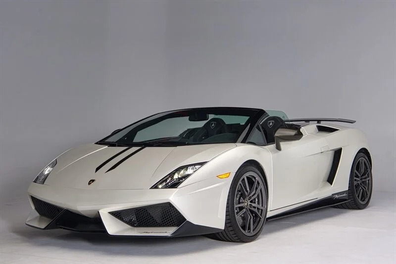 A white Lamborghini Gallardo Spyder convertible, an iconic supercar, is parked in a studio with a plain gray background.