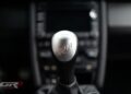 Close-up of a manual gear shift knob with "RF" engraved on top, set against the blurred center console of an ultra-rare 2012 RUF Rt 12 R.