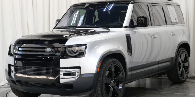 A silver and black Land Rover Defender SUV, one of the top affordable luxury SUVs, is parked indoors in front of a white curtain backdrop.
