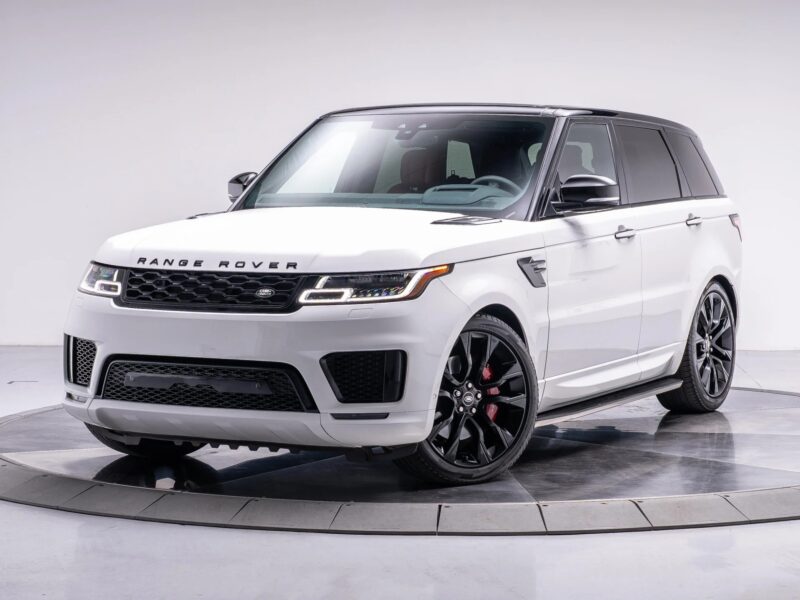 „White Range Rover“ visureigis su juodais akcentais, vaizduojančiais prieinamų prabangių visureigių viršūnę, yra pastatytas ant apskrito platformos gerai apšviestoje studijos aplinkoje.