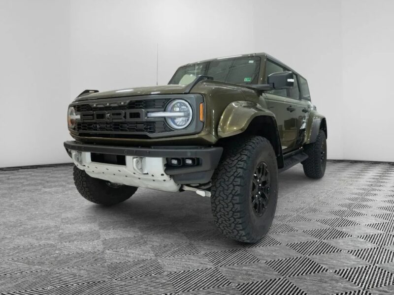 Žalias „Ford Bronco“ visureigis, vienas iš praktiškiausių visureigių, yra pastatytas baltame vidaus salone su raštuotomis grindimis, žiūrint iš priekinio kairiojo kampo.
