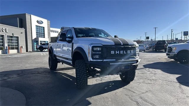 A white Shelby-modified Ford pickup truck, known for its luxury trucks comfort and impressive capability, is parked in front of a car dealership on a sunny day.
