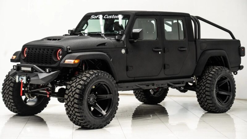Black modified Jeep Gladiator pickup truck with large off-road tires, lifted suspension, custom bumper, and roll bars, parked indoors on a white floor—a bold blend of luxury trucks comfort and outstanding off-road capability.