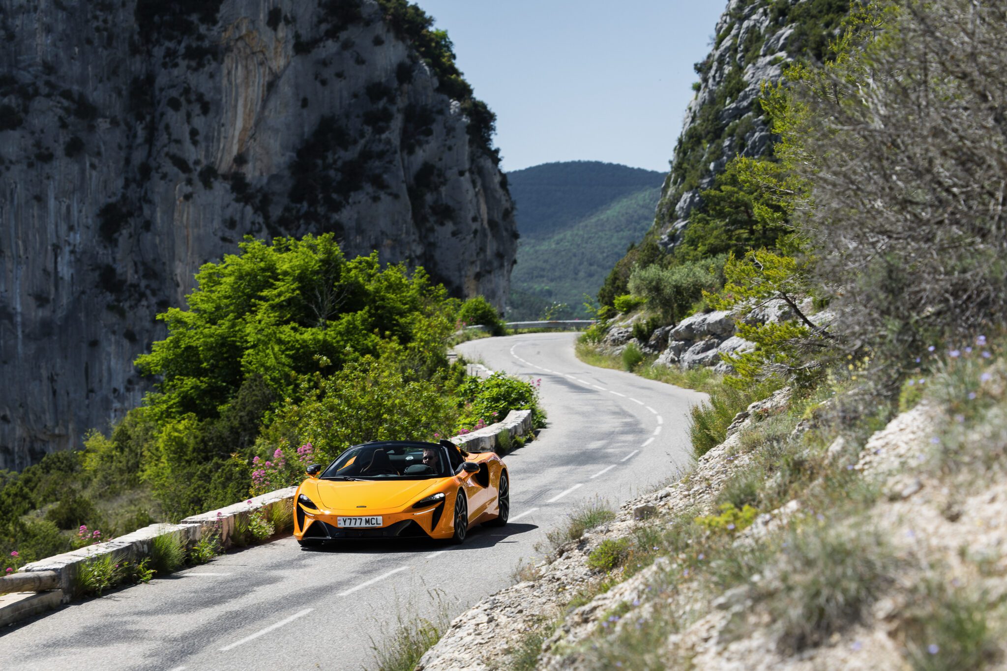 An image of a McLaren Artura Spider driving on a mountain road.