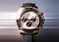 A Rolex Oyster Perpetual Cosmograph Daytona, one of the most iconic luxury chronographs, featuring a rose gold case, black bezel, and black rubber strap set against a blurred gradient background that evokes automotive elegance.