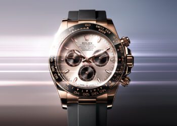A Rolex Oyster Perpetual Cosmograph Daytona, one of the most iconic luxury chronographs, featuring a rose gold case, black bezel, and black rubber strap set against a blurred gradient background that evokes automotive elegance.