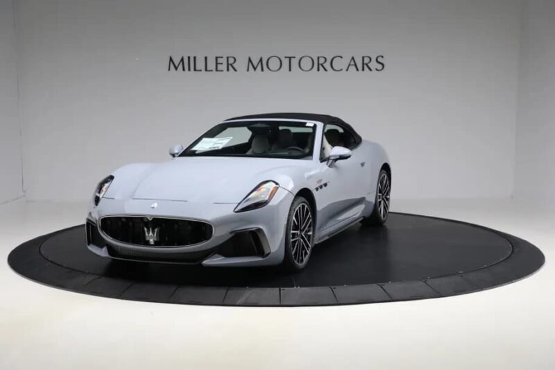 A silver Maserati convertible, epitomizing Italian luxury, is displayed on a circular platform in a showroom with "Miller Motorcars" on the wall behind it.