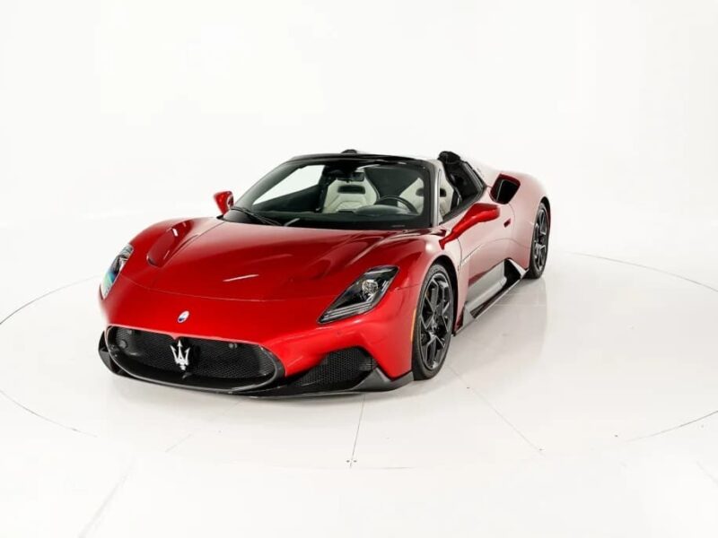 A red Maserati convertible sports car, an icon of Italian luxury, is photographed in a white studio with the top down, showcasing black wheels and sleek aerodynamic lines.
