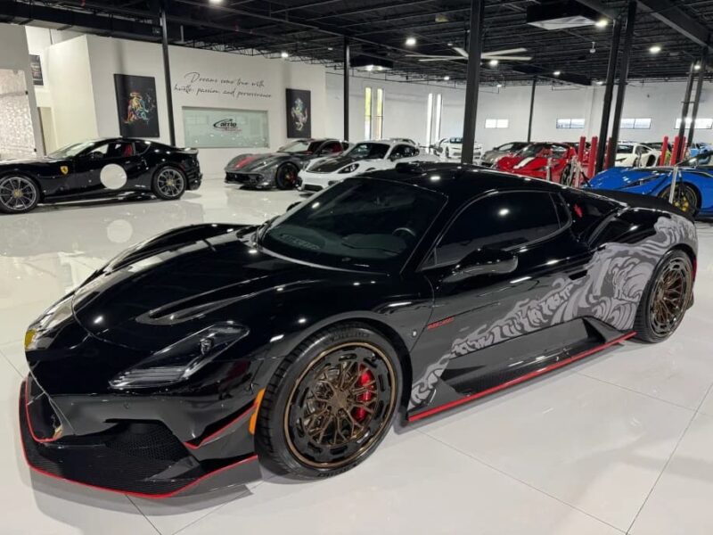A black Maserati exotic sports car with custom graphics and bronze wheels is parked in a showroom with other Italian luxury vehicles, available for sale.