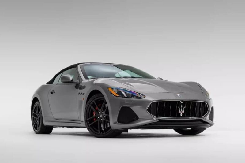 A gray Maserati GranTurismo convertible epitomizing Italian luxury is parked in a studio with a plain white background.