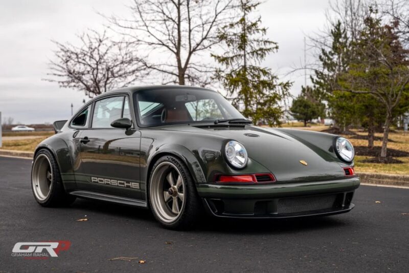 Klasikinį oru aušinamą 911 primenantis vintažinio stiliaus žalias „Porsche“ plačiais ratais stovi asfaltuotame kelyje, belapių medžių apsuptyje. Apatiniame kairiajame kampe matomas logotipas.