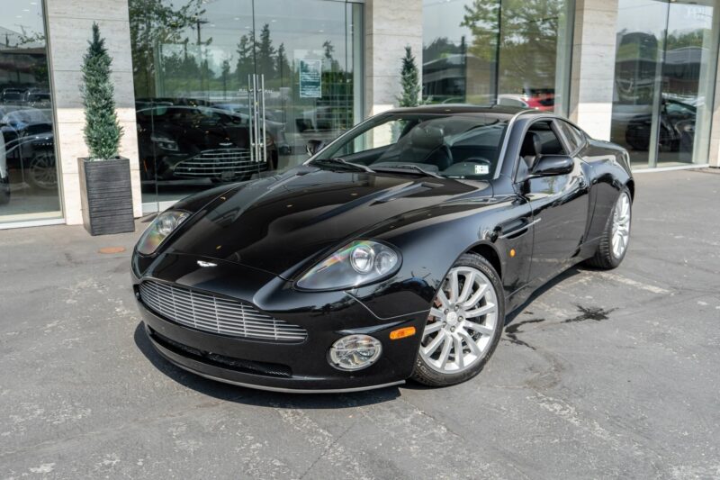 A black Aston Martin coupe, showcasing British luxury and performance, is parked in front of a modern glass building on a paved surface.