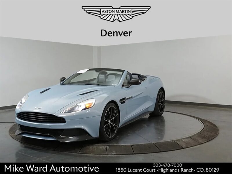 A light blue Aston Martin convertible, a true British luxury performance machine, is displayed in a showroom with a white wall at Mike Ward Automotive in Denver.