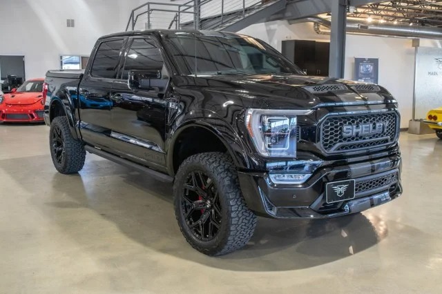 A sleek Ford F-150 Shelby pickup truck with large off-road tires is parked indoors, showcasing the epitome of rugged elegance. If you're looking to buy trucks that combine power and style, this model is a perfect choice.