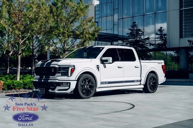 A pristine white Ford F-150 pickup truck is parked outdoors on a paved surface near trees and a building. Discover the power and elegance it offers—consider making it yours today.