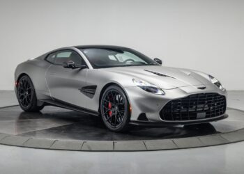A silver Aston Martin coupe, a true performance machine with black wheels and red brake calipers, is displayed in a studio with a white background.