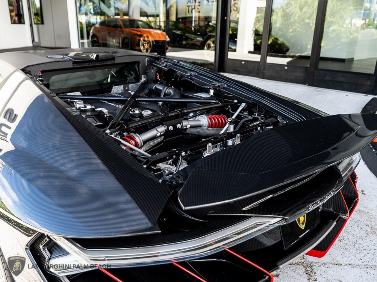 Close-up view of a 2017 Lamborghini Centenario's engine compartment, showcasing intricate components and carbon fiber details, elegantly highlighted by the stunning Giallo Midas finish.