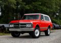 A vintage red and white GMC SUV is parked on a gravel surface with green trees in the background, perfect for classic trucks enthusiasts.