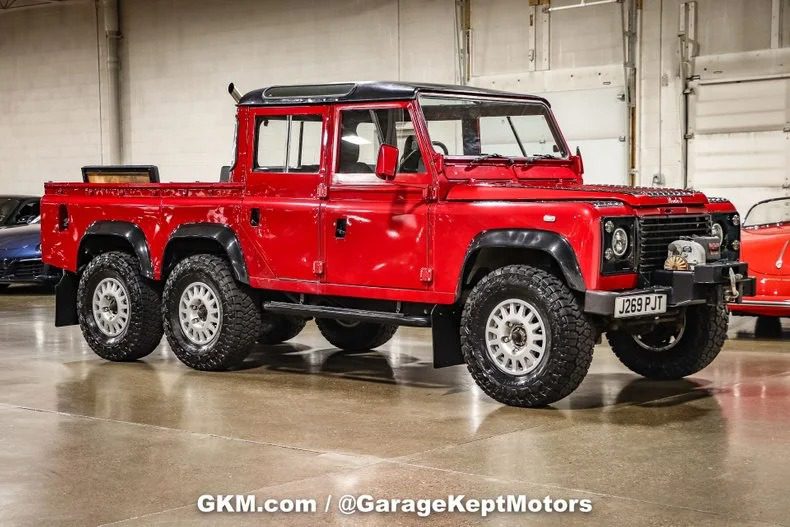 A red six-wheel drive Land Rover Defender turns heads as it sits parked indoors on a polished concrete floor.